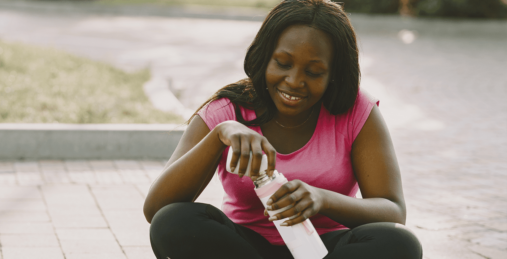 A woman takes a break from exercising to drink water from her thermos.