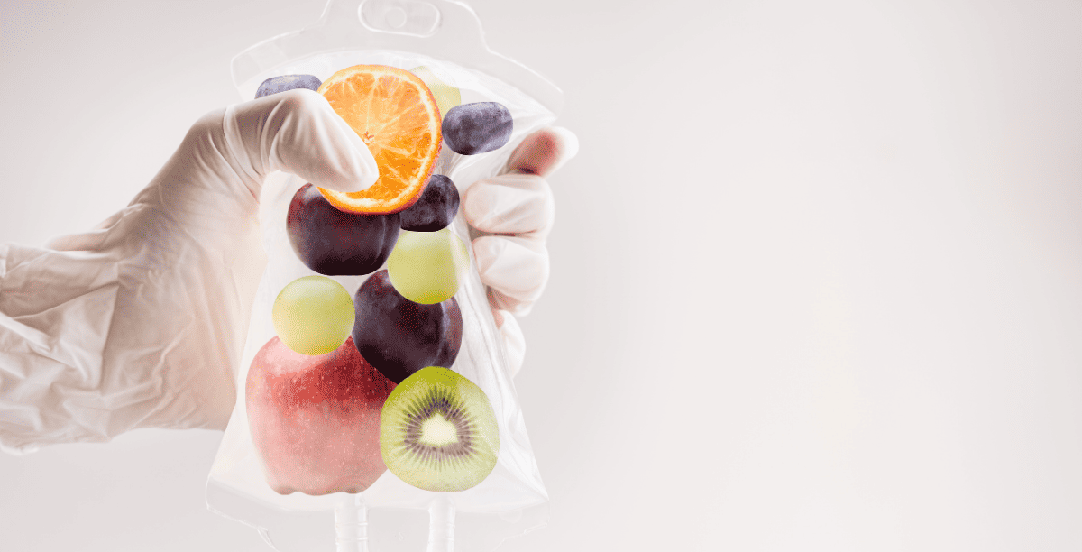 A hand holding an IV bag with various fruits inside