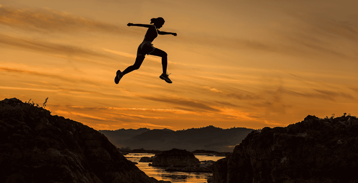 woman leaping between mountain tips at sunset 