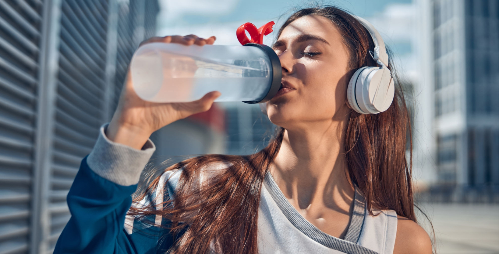 Woman sits on floor with bowl of salad on her lap and exercise weights on the floor in front of her.