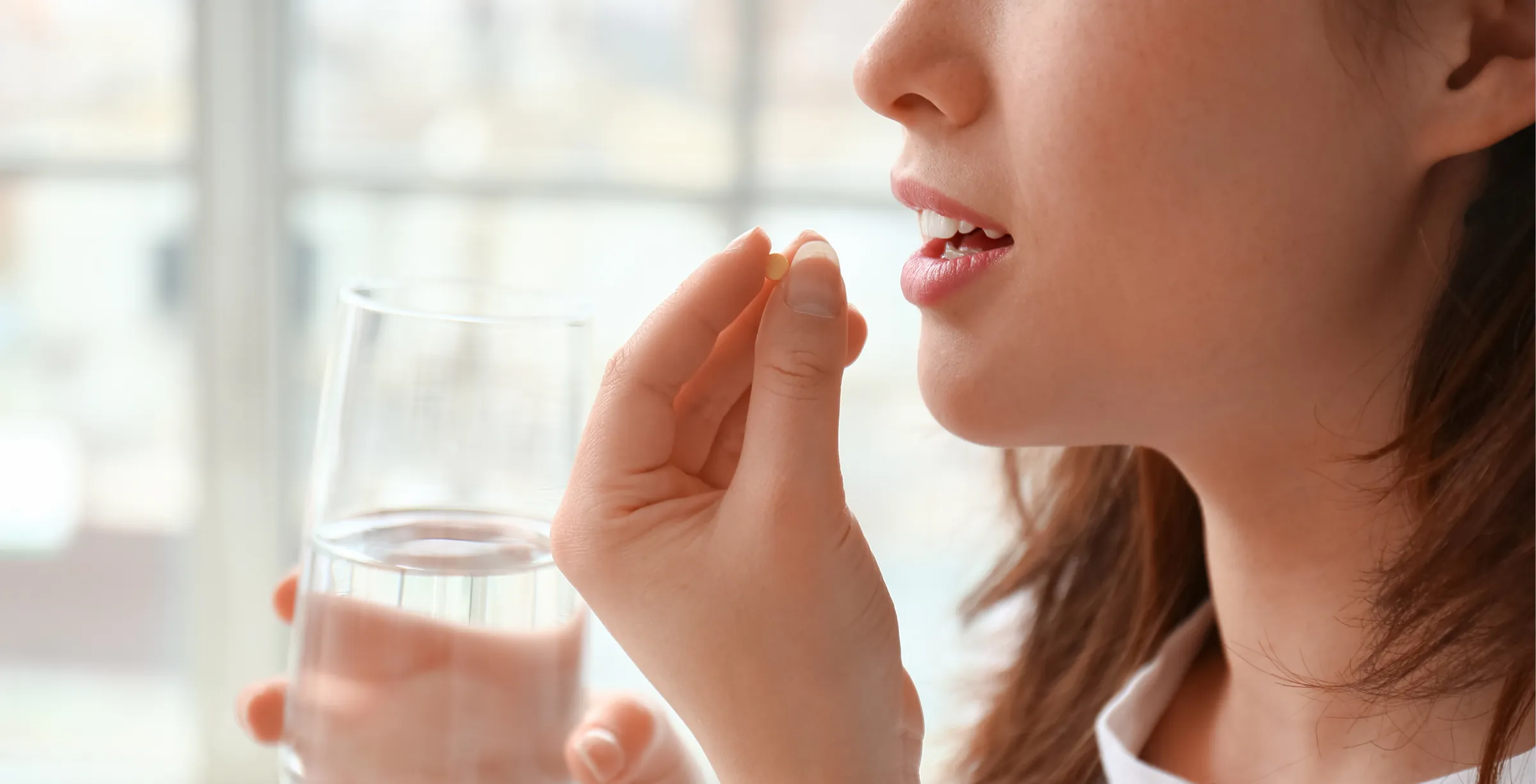 Woman putting small pill into her mouth